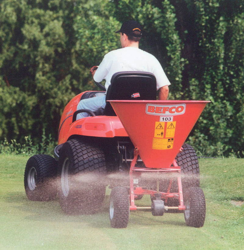 BEFCO spreader in action, attached to a lawn tractor, distributing material evenly across a grassy area