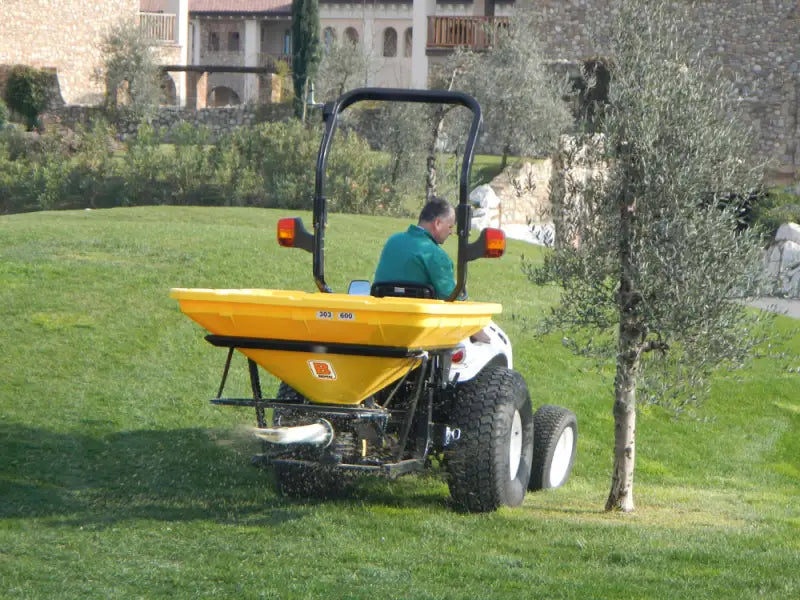 Operator using BEFCO Turbo-Hop 303 spreader on a tractor, spreading material on a grassy landscape.
