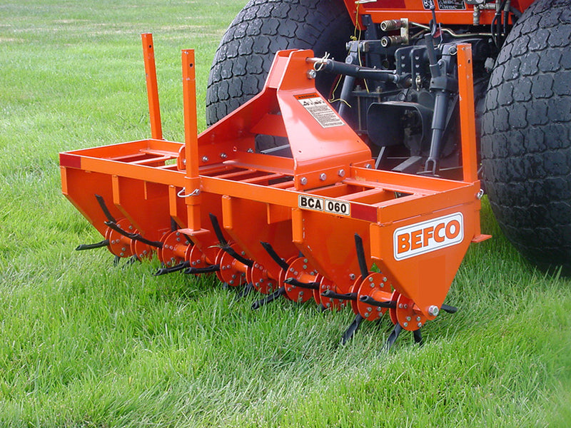 BEFCO core aerator attached to a tractor, operating on grass, showcasing its sturdy steel construction.