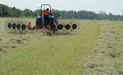 BEFCO V wheel hay rake in action, attached to a tractor, efficiently raking hay into uniform windrows.
