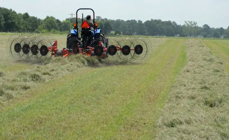 BEFCO V wheel hay rake in action, attached to a tractor, efficiently raking hay into uniform windrows.