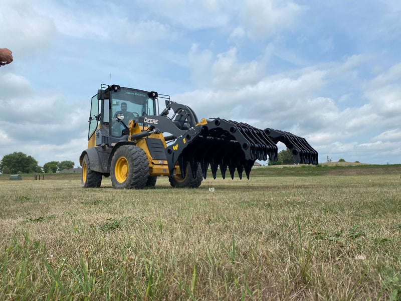 Yellow John Deere tractor with open black Stinger attachment claw angled down