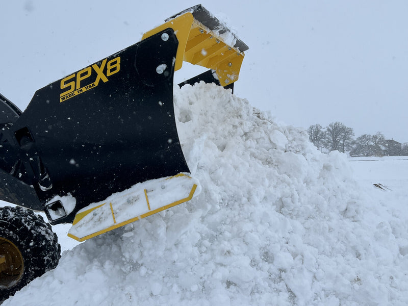 Side view of SPX8 snow pusher moving a large snow pile, highlighting its capacity and strength.