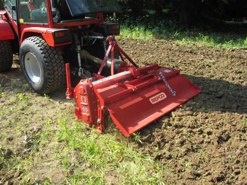 BEFCO rotary tiller attached to a tractor, efficiently tilling soil in a field, demonstrating practical use.
